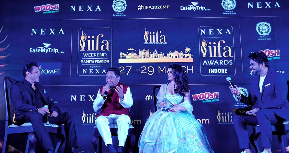 The illustration has a dark blue background with the iifa logo in the centre below the logo; there is "27-29 MARCH" text in golden. There are multiple logos of sponsor brands in the background and four guests sitting on the chair.