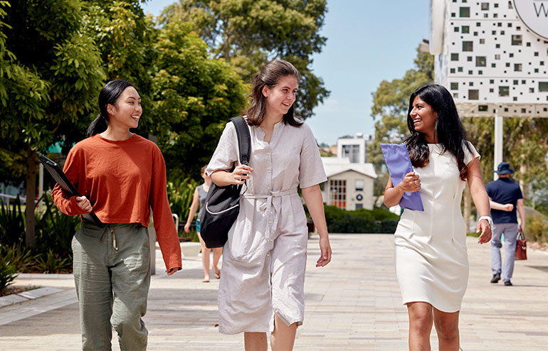 The image shows three girls students walking on the college campus.