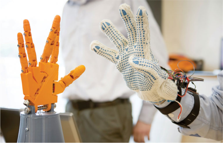The image with a blurred background shows one robotic hand and one human hand.