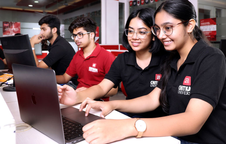 The image shows the four students of chitkara university, three in black t-shirts and one in red, working on laptops.