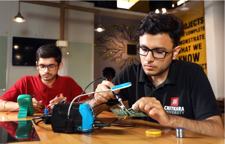 the illustration shows the two mechatronics engineering students from chitkara university—one in a black t-shirt other in red working on their projects.