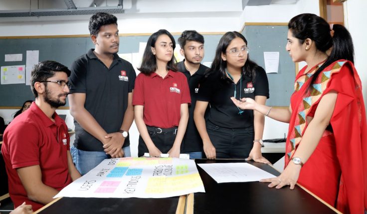 Four students collaborating and learning UI/UX Design, discussing design concepts on a laptop.