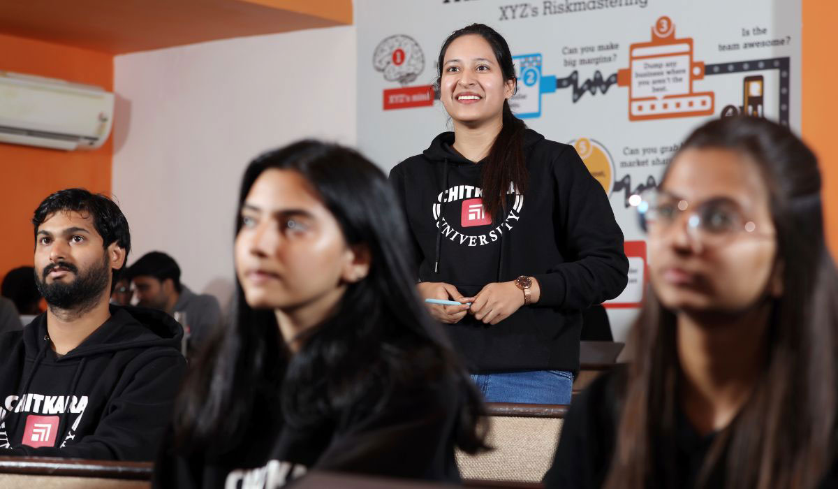 A girl standing in a classroom confidently answering a question about MBA in Finance to the teacher.