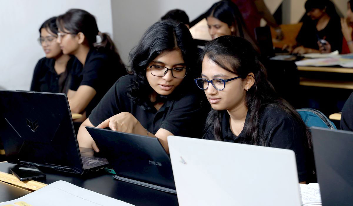 Two female students discussing and working on a laptop, representing collaboration and learning in a BBA in Analytics and Big Data program focused on data analysis and corporate leadership.