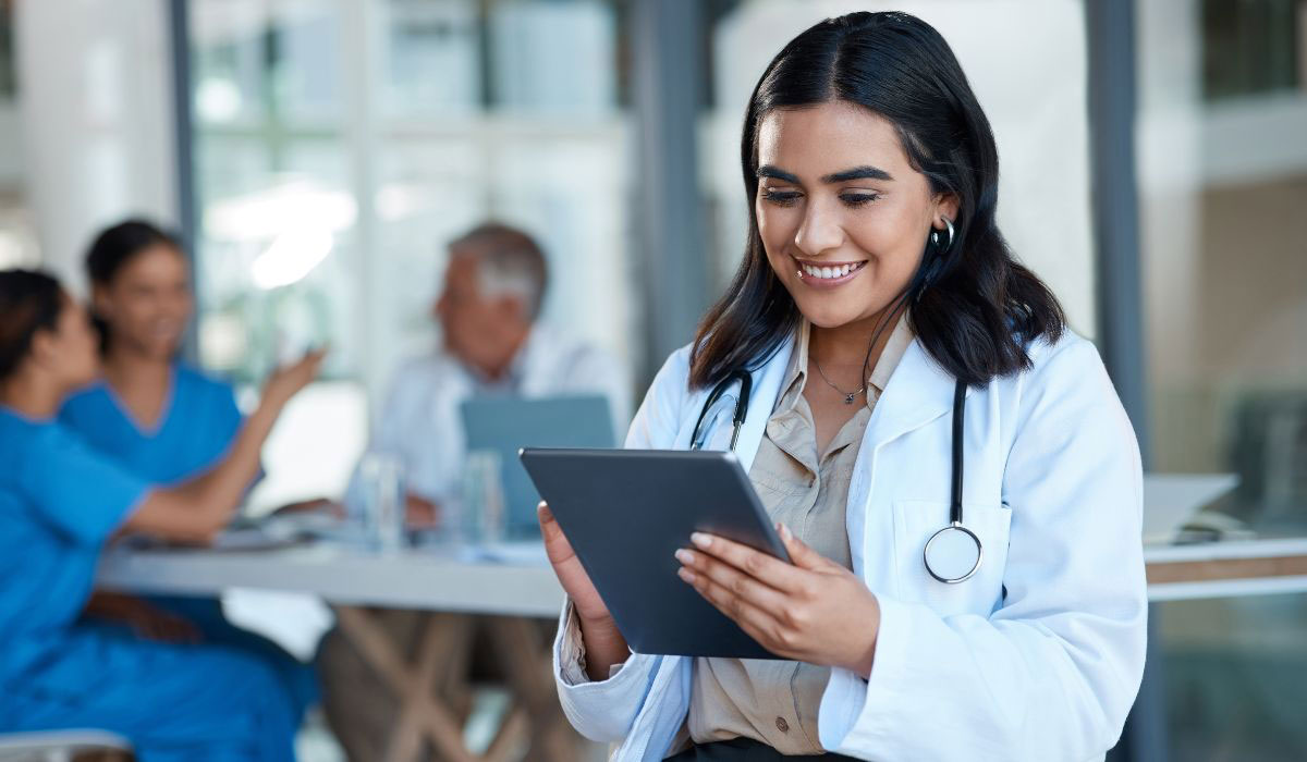 A smiling healthcare professional in a white coat using a digital tablet, symbolizing the growing role of Digital Health Solutions in modern healthcare management.
